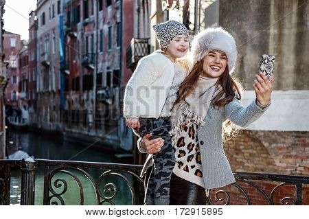 Venice. Off the Beaten Path. happy modern mother and child tourists in Venice Italy in the winter with mobile phone taking selfie