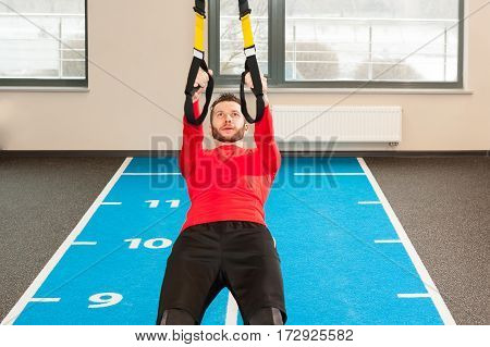 white curly bearded sporty man exercising with fitness straps in gym