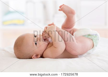 baby lying on white sheet and sucking his foot