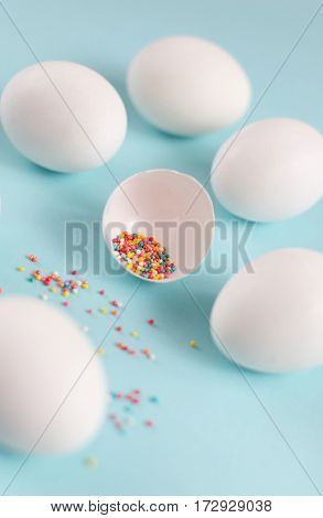 Easter decoration white chicken eggs and broken egg with colored sugar ingredients on a light blue background vertical image
