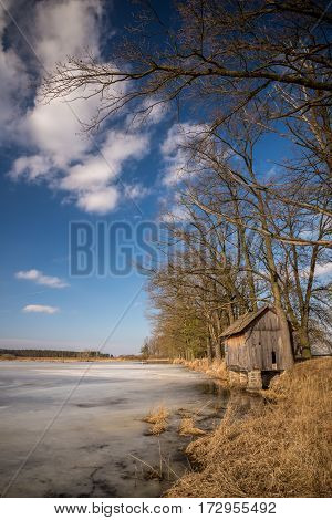 Early Spring Scene Of Partially Frozen Pond With Old Hut
