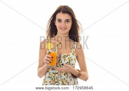 cheerful brunette woman in sarafan with floral patter drinks fresh orange cocktail and smiling on camera isolated on white