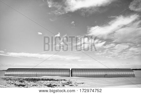 Two industrial steel culverts laying on snow covered field in a black and white winter landscape