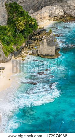 Rock in the ocean with beautiful palms behind at Atuh beach on Nusa Penida island, Indonesia.