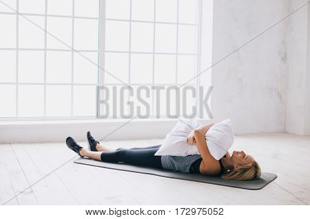 Young woman laying on a mat with pillow and she is hugging it. Yoga girl having some rest doing breath or relaxing exrcises