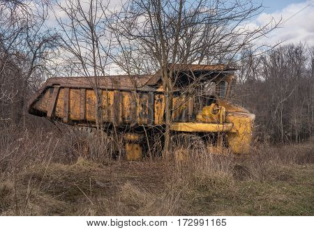 Rusting and overgrown heavy yellow industrial truck and equipment abandoned in economic recession