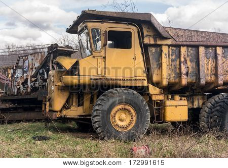 Rusting and overgrown heavy yellow industrial truck and equipment abandoned in economic recession