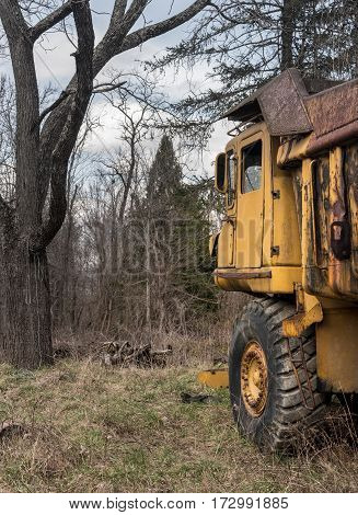 Rusting and overgrown heavy yellow industrial truck and equipment abandoned in economic recession