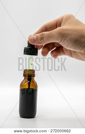 Hand Holding The Dropper With Green Color  Over The Amber Glass Bottle Isolated On White