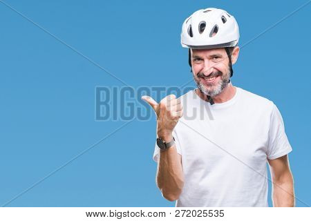 Middle age senior hoary cyclist man wearing bike safety helment isolated background smiling with happy face looking and pointing to the side with thumb up.
