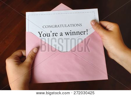A Letter That Says Congratulations You're A Winner! With Female Hands Holding The Open Pink Envelope