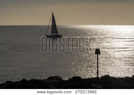 Silhouette Of Sailing Ship During Sunset At The Shore Of The Beach With Beacon, England.