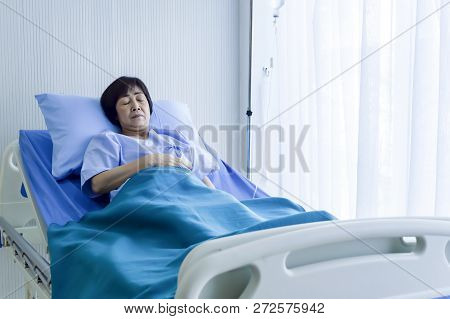 Older Sick Woman Patient Lay On Bed In Hospital With Intravenous Normal Saline. Medical Professional