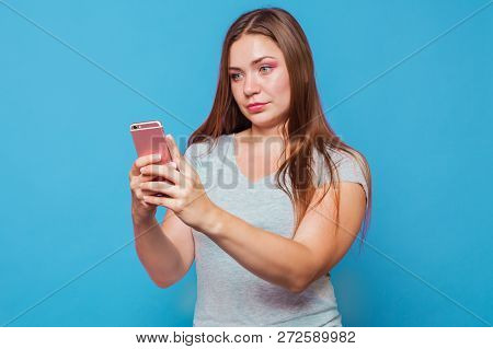 Young Caucasian Woman With Brown Hair And Blue Eyes Looks To The Pink Mobile Phone With Astonish Gri