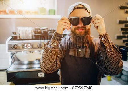 Cool Young Barista Stand Nd Pose On Camera. He Wears Sunglasses In Kitchen. Guy Smiles. He Looks Hap