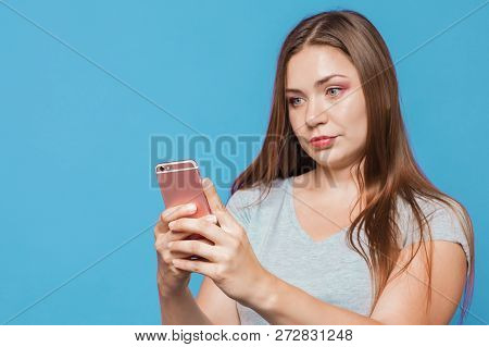 Young Attractive Caucasian Woman With Brown Hair And Bright Blue Eyes Looks To The Pink Mobile Phone