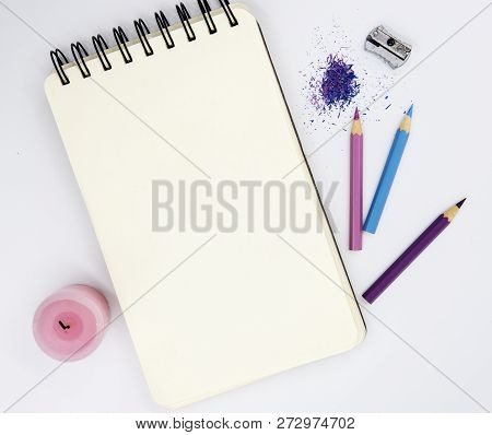 Blank Sketchbook With Pink Violet Pencils, And Sharper White Background. Artist Table Top View Photo