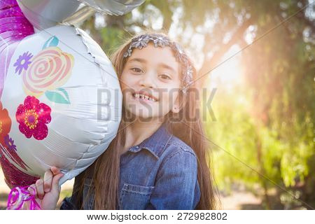 Cute Young Mixed Race Girl Holding Mylar Balloon Outdoors.