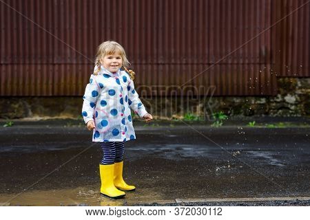 Little Toddler Girl Wearing Yellow Rain Boots, Running And Walking During Sleet On Rainy Cloudy Day.