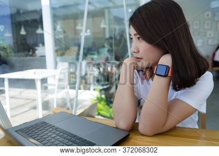 Young Asian Woman Working On Laptop Showing Smartwatch Screen Display In Cafe, Looking Away With Cop