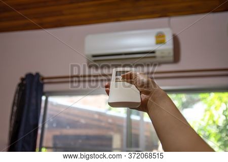 Woman Hand Holding Remote Control Directed To Air Conditioner Adjust Cold Temperature, Close Up.
Wom