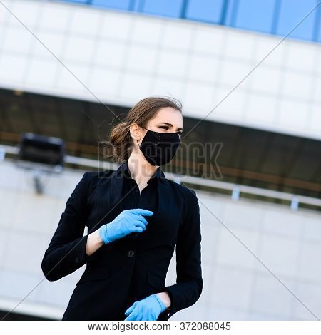 Beautiful Businesswoman In A Black Suit In A Black Medical Mask And Gloves At The City In Quarantine