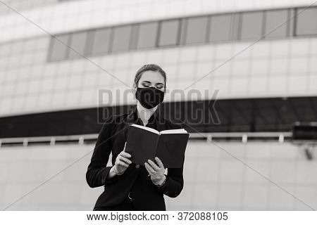 Beautiful Businesswoman In A Black Suit In A Black Medical Mask And Gloves At The City In Quarantine
