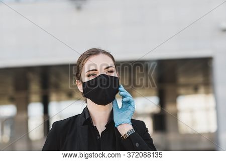 Beautiful Businesswoman In A Black Suit In A Black Medical Mask And Gloves At The City In Quarantine