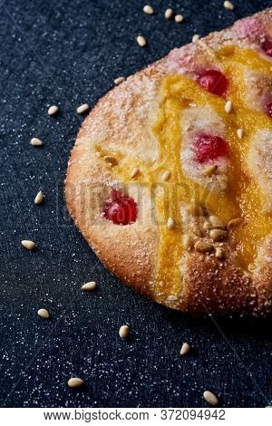 closeup of a coca de Sant Joan, a typical sweet flat cake from Catalonia, Spain, eaten on Saint Johns Eve, on a black fabric surface sprinkled with pine nuts