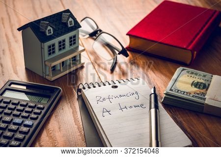 refinancing words on notebook with us dollars and stuff on wooden desk.