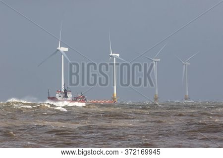 Ship On Rough Sea Horizon By Offshore Wind Farm Turbines. Safety Standby Rescue And Maintenance Vess