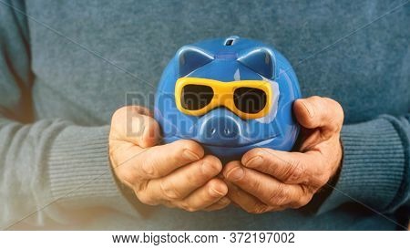 Pensioner In Blue Woolen Pullover Holds Money Box Of Pig Shape With Yellow Sunglasses In Hands Under