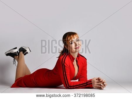 Young Pretty Smiling Red-haired Woman In Casual Sport-style Red Dress And Sneakers Is Lying On Stoma