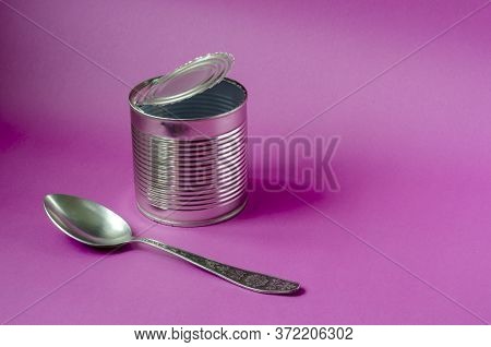 Empty Tin Can And Spoon On A Purple Background. Tin Can And Metal Spoon. Canned Food. Close-up. Copy