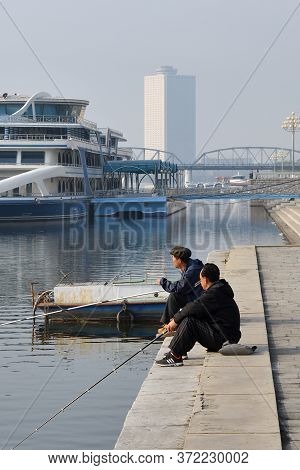 Pyongyang, North Korea - May 1, 2019: Street Scene. Two Fishermen Catch A Fish On Waterfront On Kim 