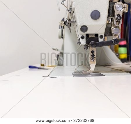 A Professional Sewing Machine Is In The Workshop. Against The Background Of Various Devices And What
