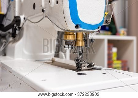 A Professional Sewing Machine Is In The Workshop. Against The Background Of Various Devices And What