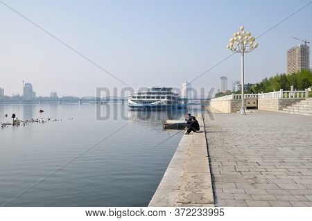 Pyongyang, North Korea - May 1, 2019: Street Scene. Two Fishermen Catch A Fish On Waterfront On Kim 