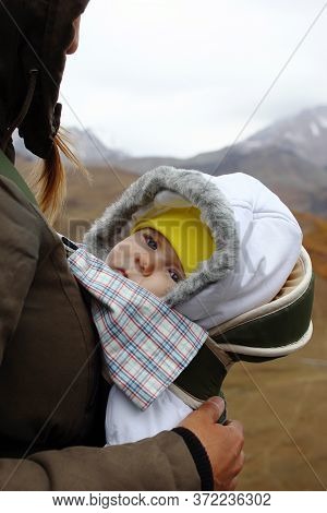 Portrait Of Little Girl In Ergo Carrier With Her Mother On A Background Of Autumn Mountains.