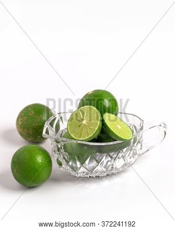Whole And Slice Green Limes In Glass Cup On White Background.