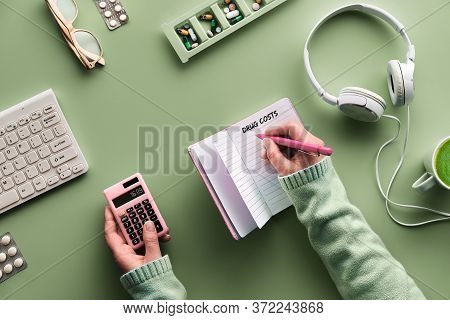 Flat Lay With Notebook To Monitor Drug Costs. Hands With Pen And Calculator. Various Pills And Pill 