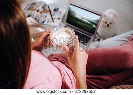 A Girl In Pajamas At Home Is Working On A Laptop With Her Dog Spitzer, The Dog And Its Owner Are Res