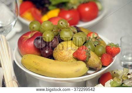 Fruit Bowl With Strawberries And Kiwi Grapes, Wine And Bananas On A Table With White Tablecloth