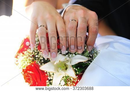 A Newly Weding Couple Place Their Hands On A Wedding Bouquet Showing Off Their Wedding Rings.