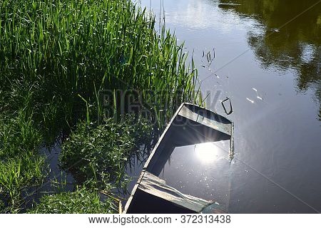 Old Wooden Boat Flooded Near The Shore And The Reflection Of The Sun In The Water.
