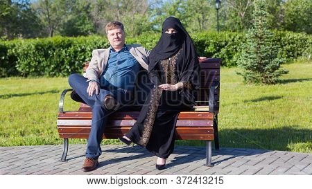 Caucasian Man And Islamic Woman Chatting On The Street. A European Adult Man Tells A Funny Story To 