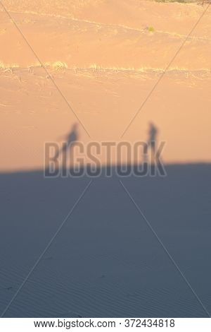 Two Explorers On The Desert, Casting Shadows On The Sand Dunes On A Hot, Sunny Day.