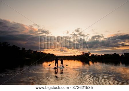 Beautiful View Of Sunset And River On Which Pair Of People Swim On The Sup Boards