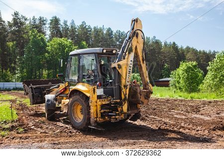 Clearing And Leveling A Private Land Plot. Yellow Excavator Driven Earth In A Wide Bucket, Back View
