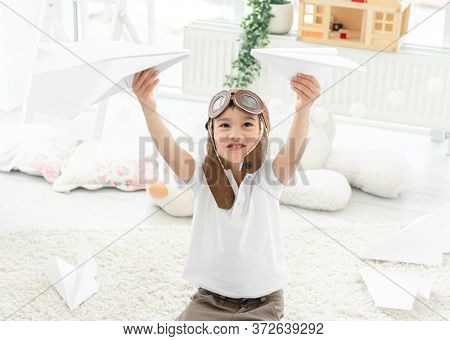 Funny little boy in pilot hat playing with paper planes in light room